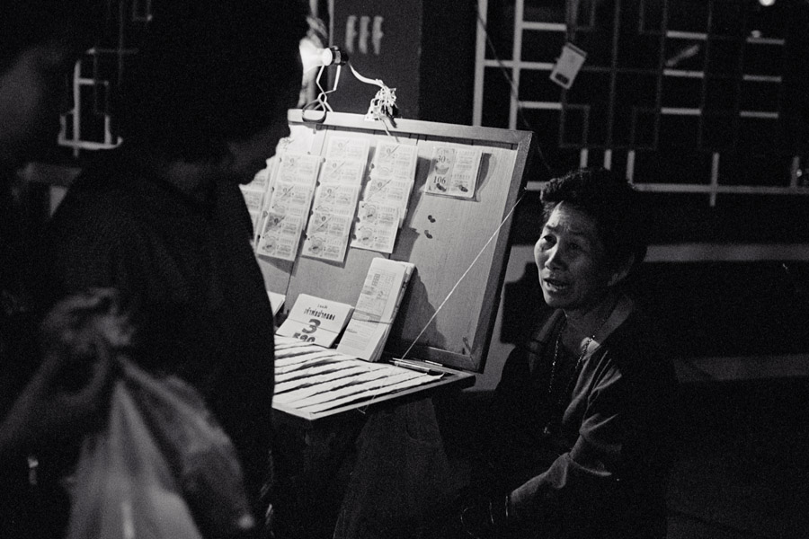 2011: Lottery seller at a night market. Burmese people play two additional games where bets are made on the last 2 or last 3 numbers of the winning ticket in the Thai lottery.